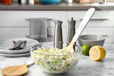 Photo of Bowl with fresh cabbage salad on marble table in kitchen