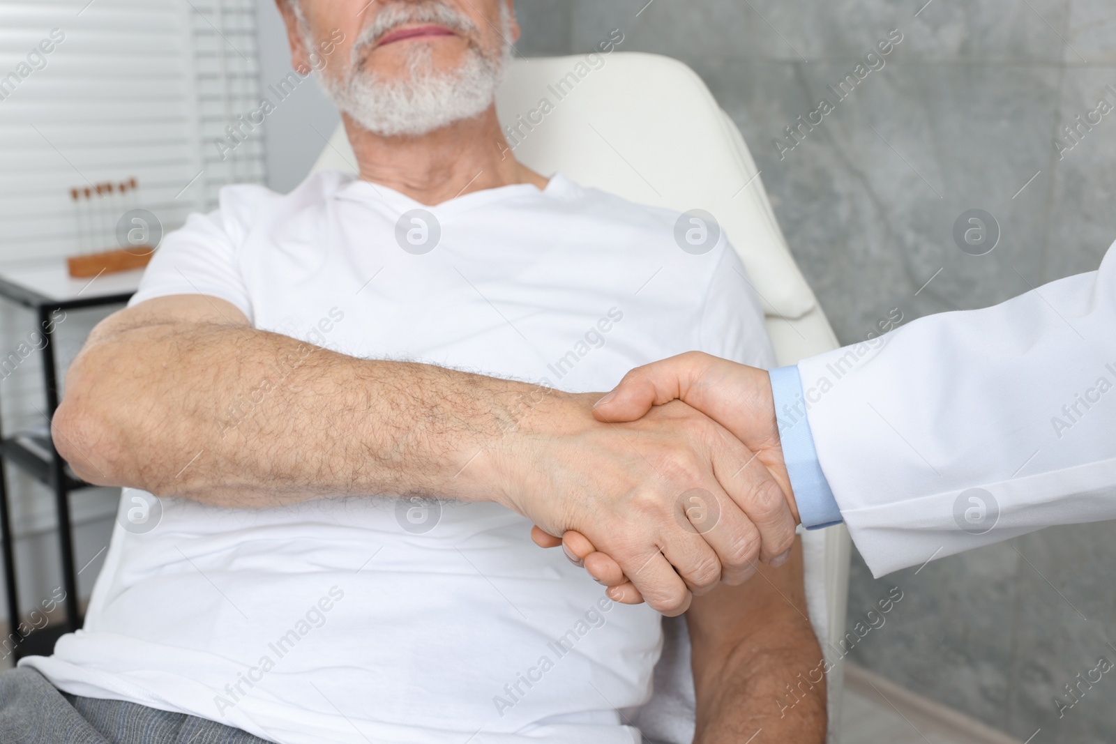 Photo of Doctor shaking hands with senior patient in hospital, closeup