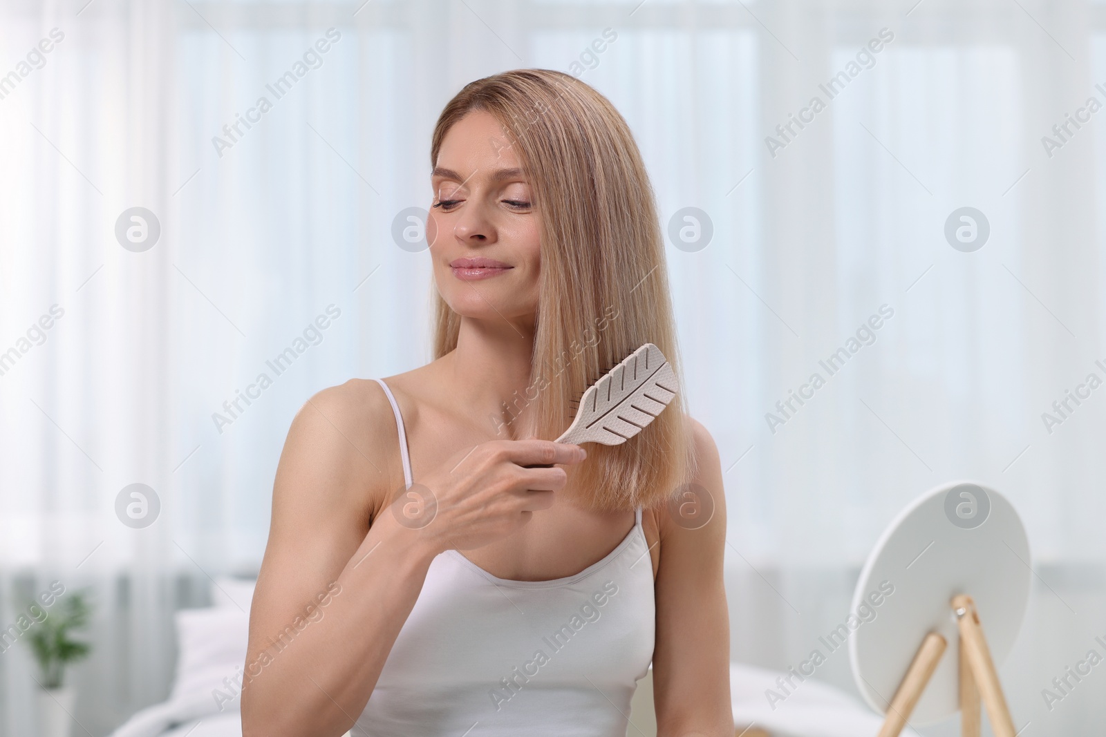 Photo of Beautiful woman brushing her hair in bedroom