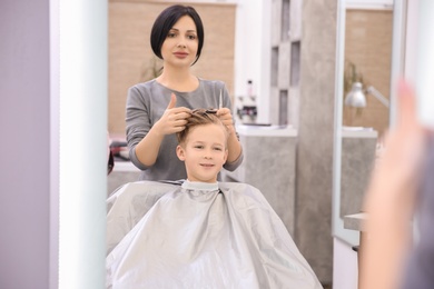 Photo of Professional female hairdresser working with little boy in salon