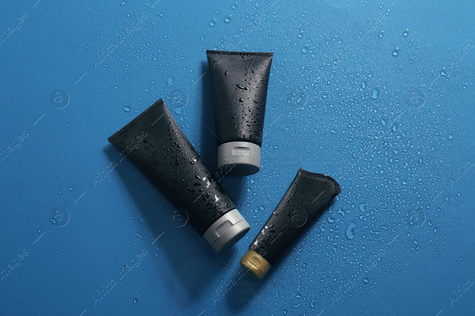 Photo of Black tubes with space for design on wet color surface, flat lay. Men's cosmetic products