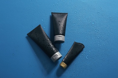 Photo of Black tubes with space for design on wet color surface, flat lay. Men's cosmetic products