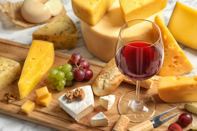 Photo of Board with different kinds of delicious cheese, snacks and wine on marble table