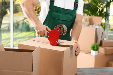 Photo of Man packing box with adhesive tape indoors, closeup. Moving service