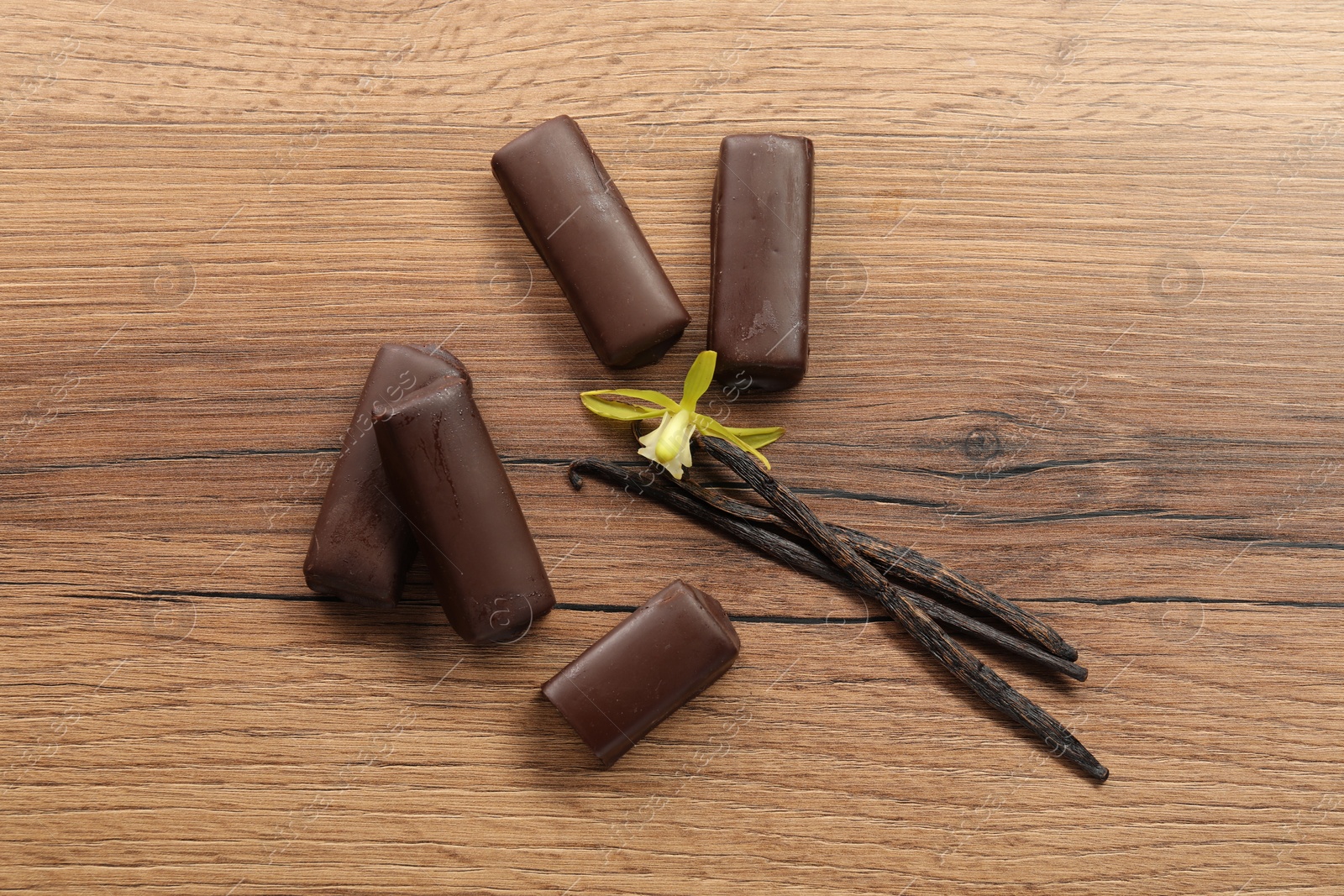 Photo of Glazed curd cheese bars, vanilla pods and flower on wooden table, flat lay