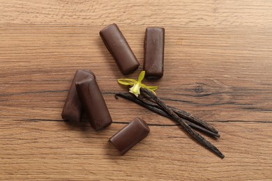 Glazed curd cheese bars, vanilla pods and flower on wooden table, flat lay