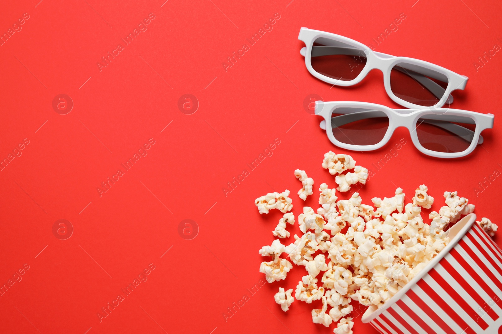 Photo of Overturned paper cup with delicious popcorn and 3D glasses on red background, flat lay. Space for text