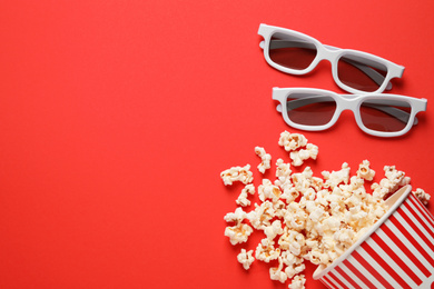 Photo of Overturned paper cup with delicious popcorn and 3D glasses on red background, flat lay. Space for text