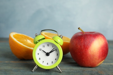 Photo of Alarm clock, orange and apple on light blue wooden table. Meal timing concept