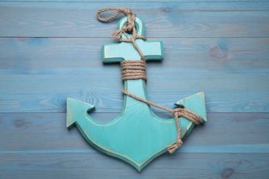 Anchor with hemp rope on light blue wooden table, top view