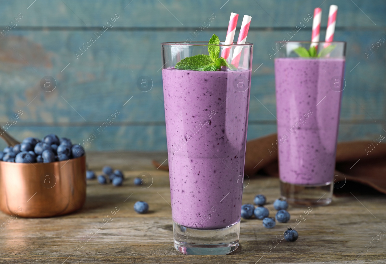 Photo of Glasses of delicious blueberry smoothie on wooden table against blue background