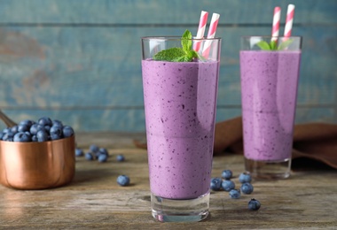 Glasses of delicious blueberry smoothie on wooden table against blue background