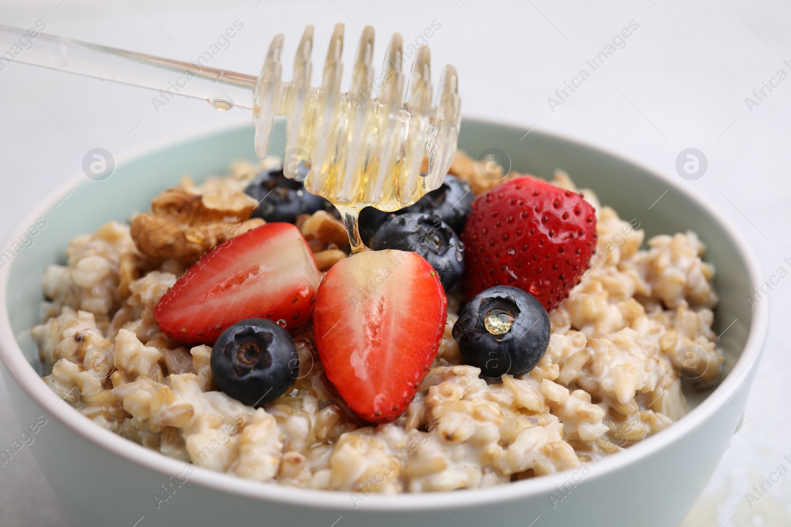 Photo of Tasty oatmeal with strawberries, blueberries and walnuts in bowl on grey table, closeup