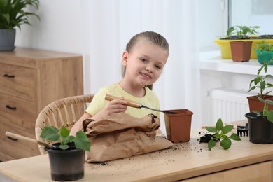 Cute little girl planting seedling into pot at wooden table in room