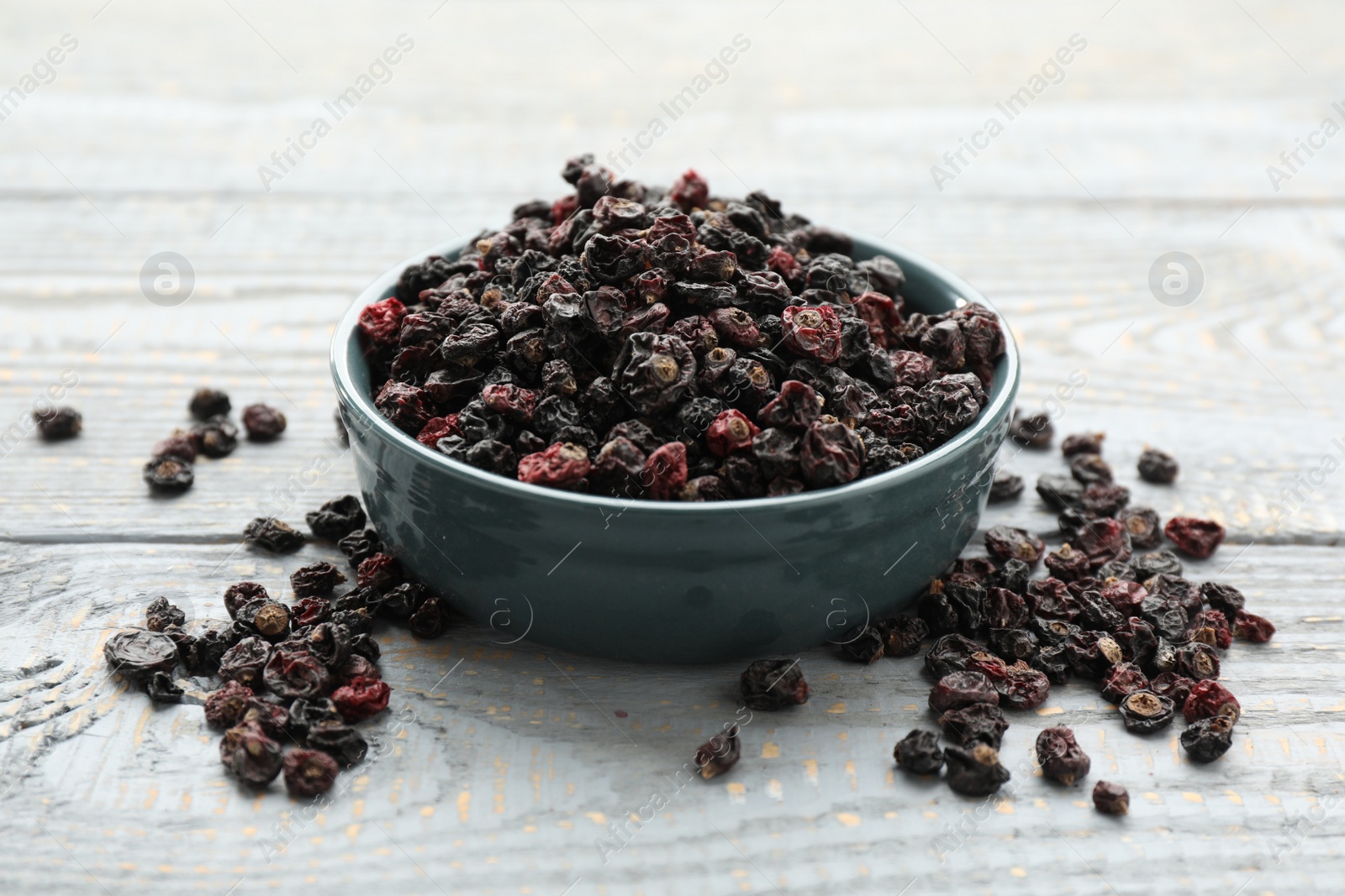 Photo of Dried black currants and bowl on grey wooden table