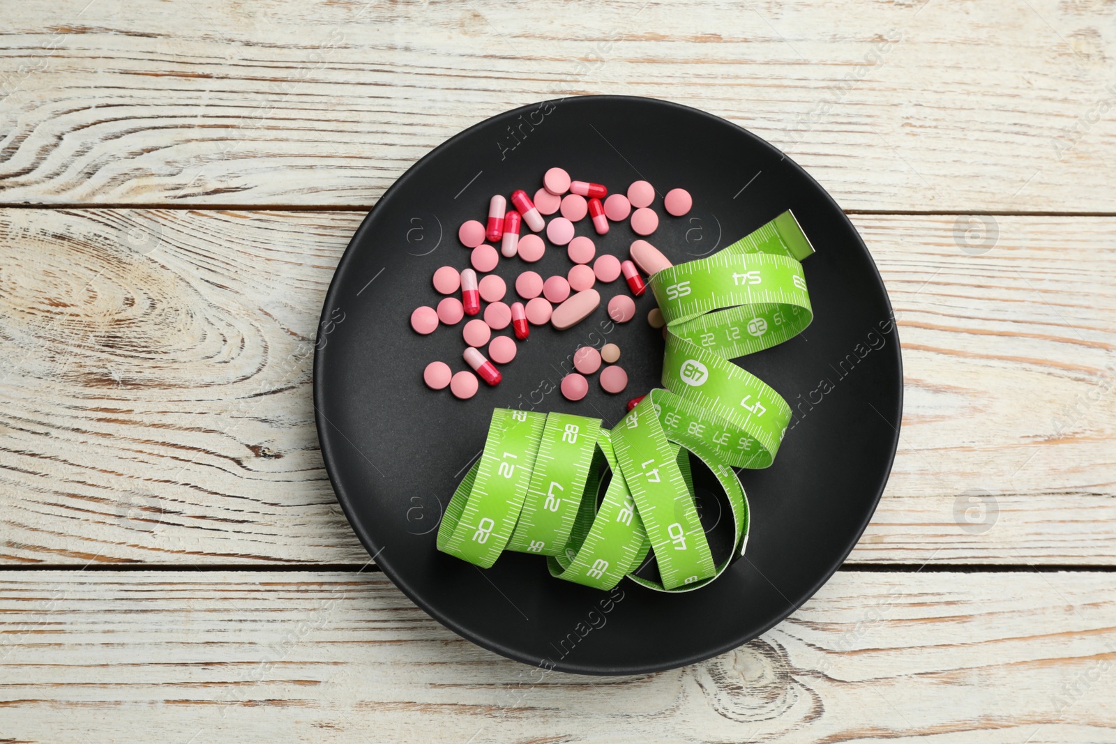 Photo of Plate with weight loss pills and measuring tape on white wooden table, top view