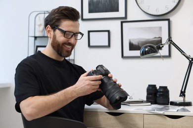 Professional photographer in glasses holding digital camera at table in office