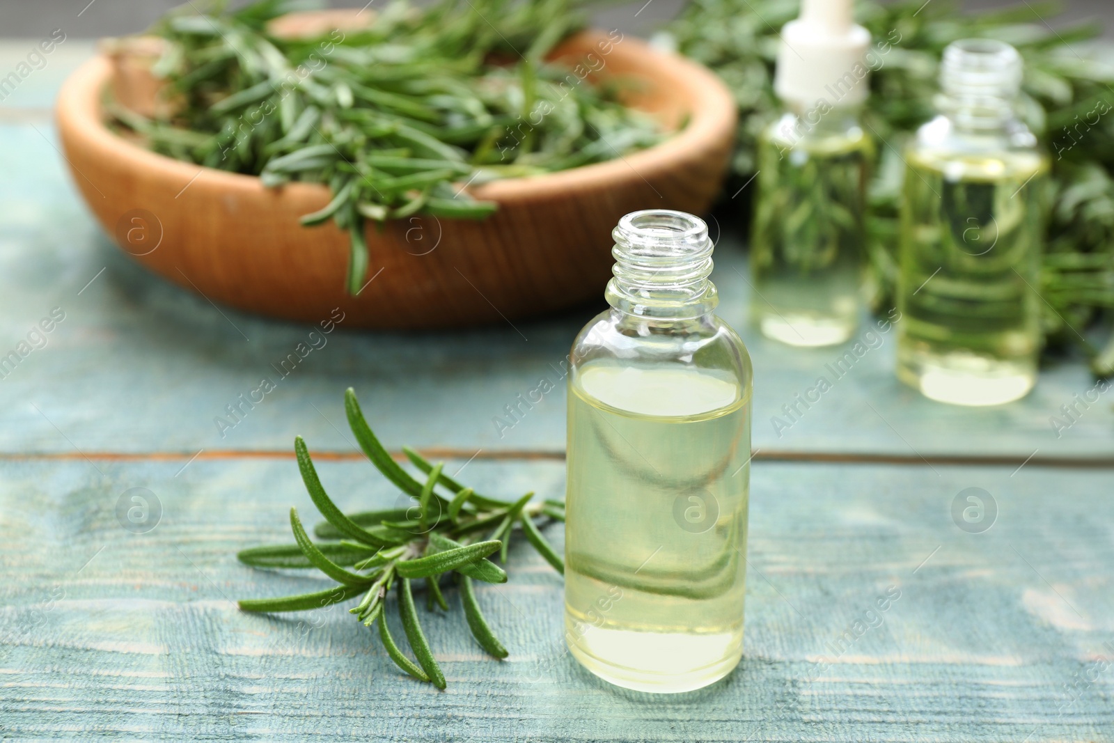 Photo of Fresh rosemary and bottle of essential oil on light blue wooden table