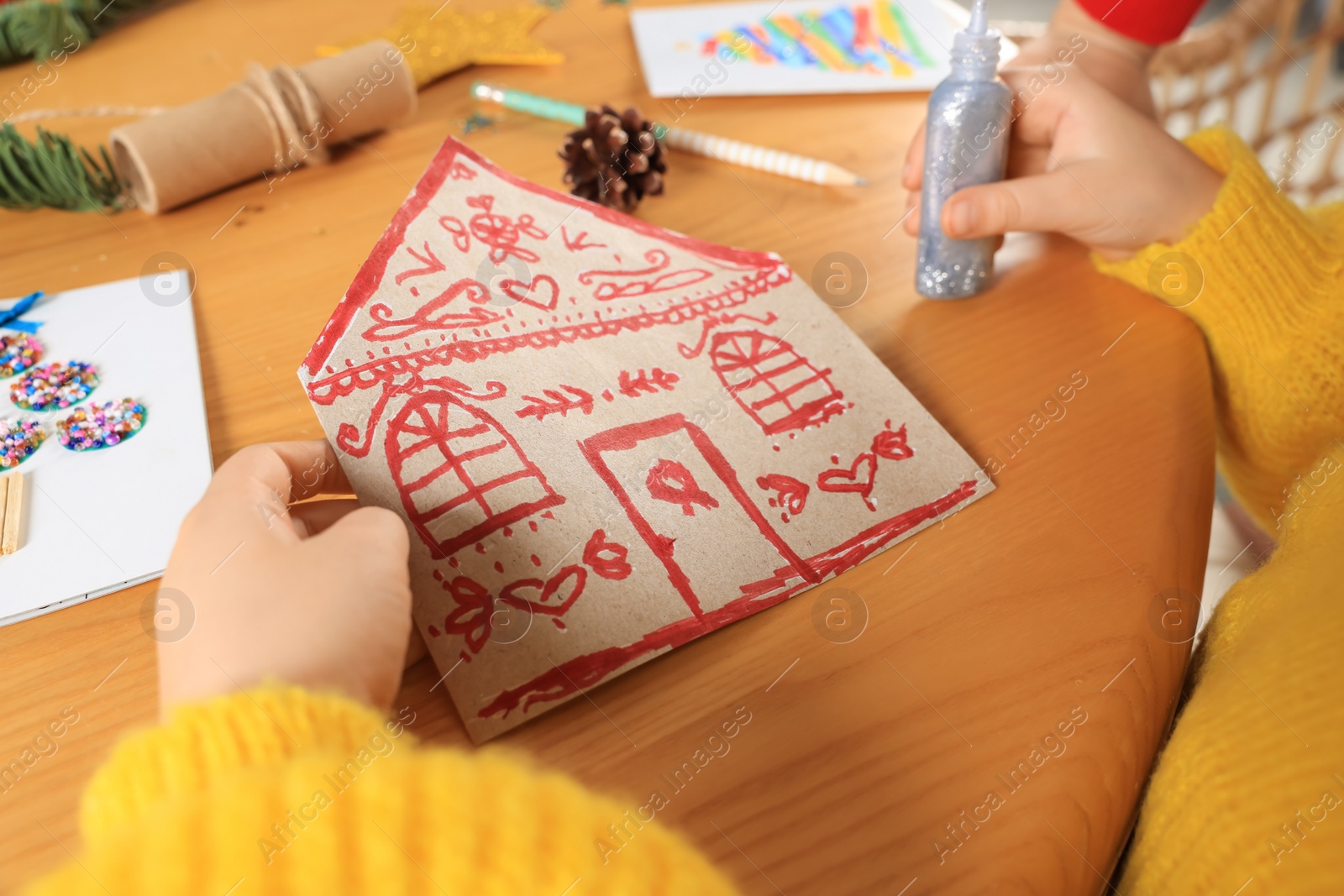 Photo of Cute little child making beautiful Christmas greeting card at wooden table, closeup