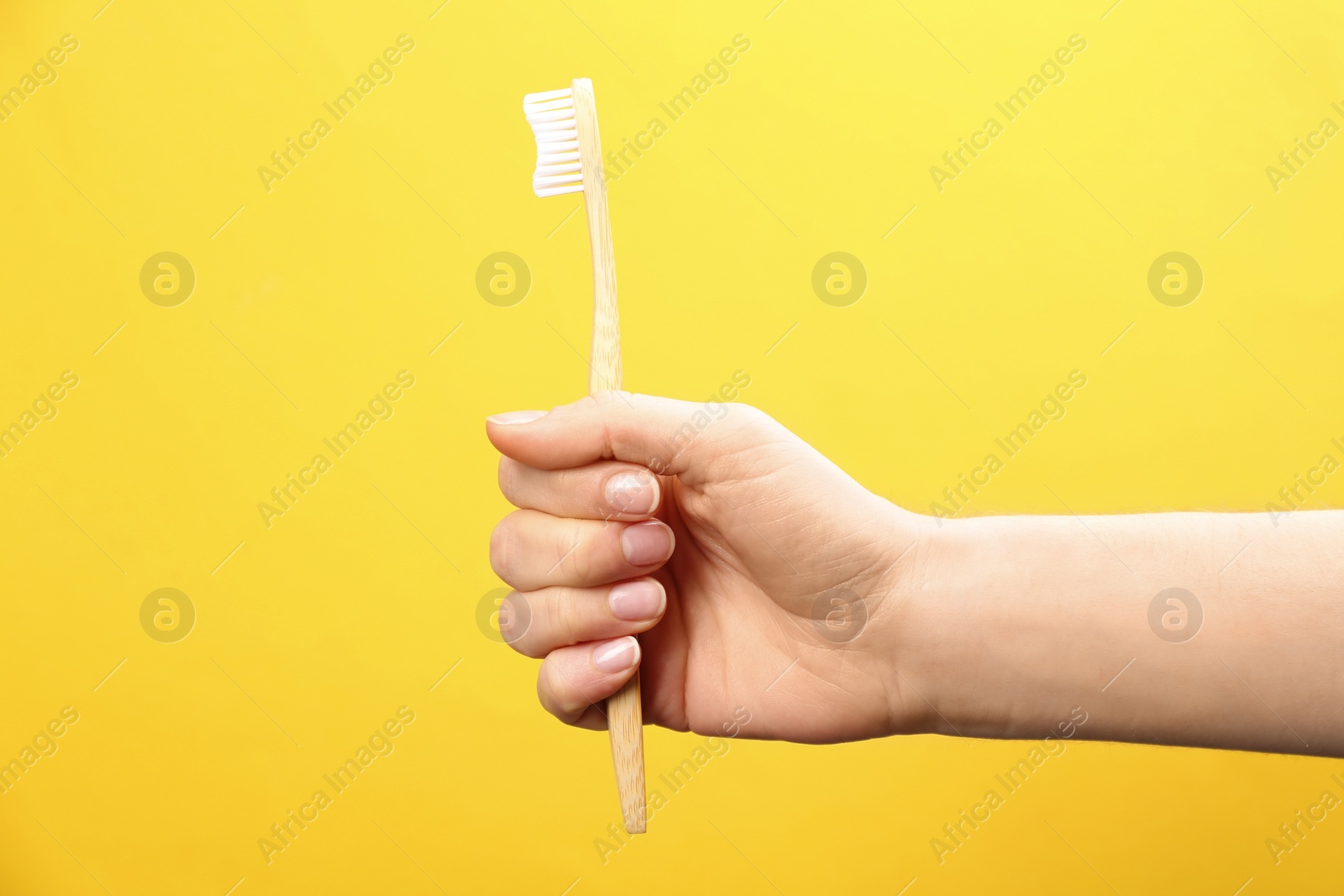 Photo of Woman holding bamboo toothbrush on yellow background, closeup