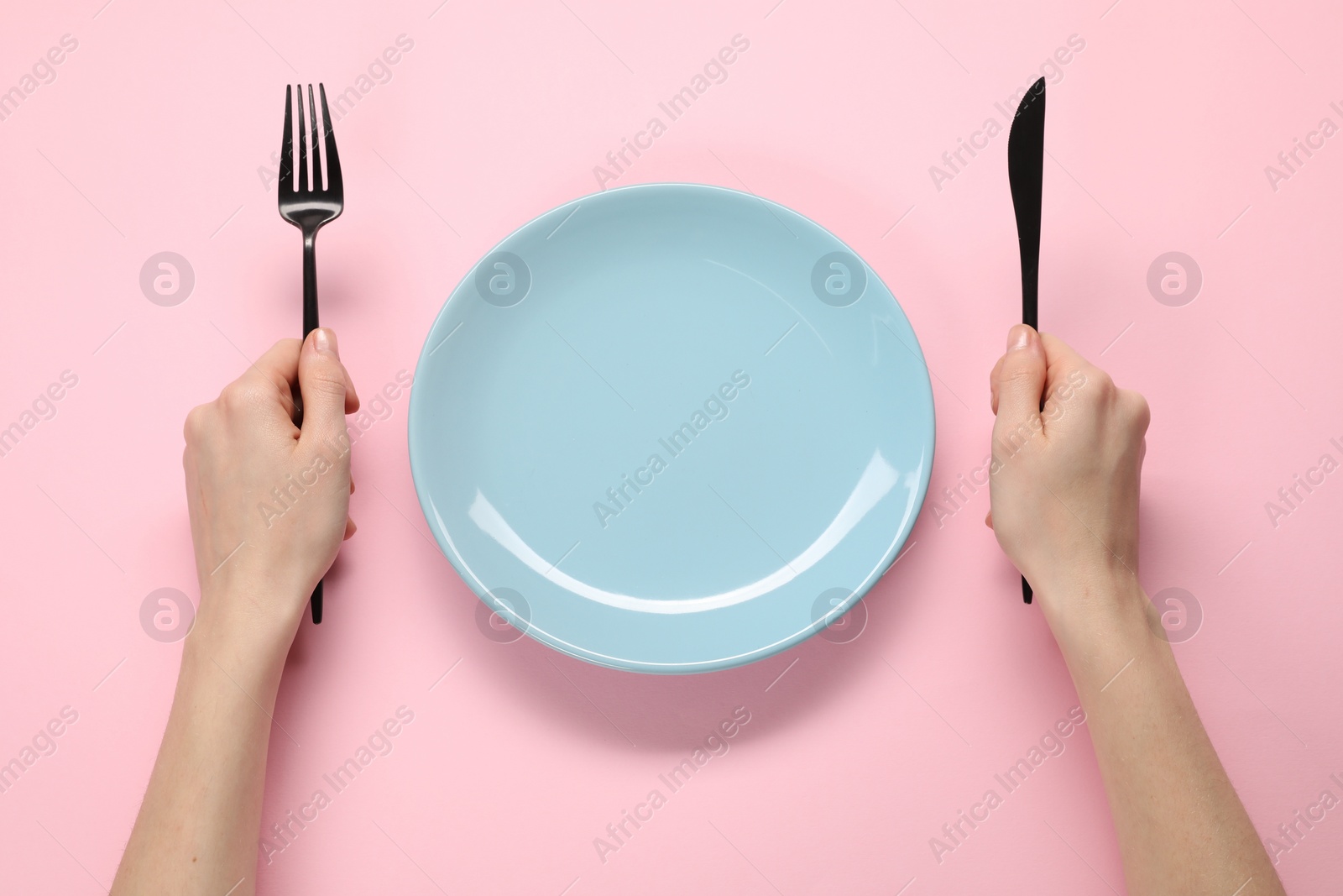 Photo of Woman with fork, knife and empty plate at pink table, top view