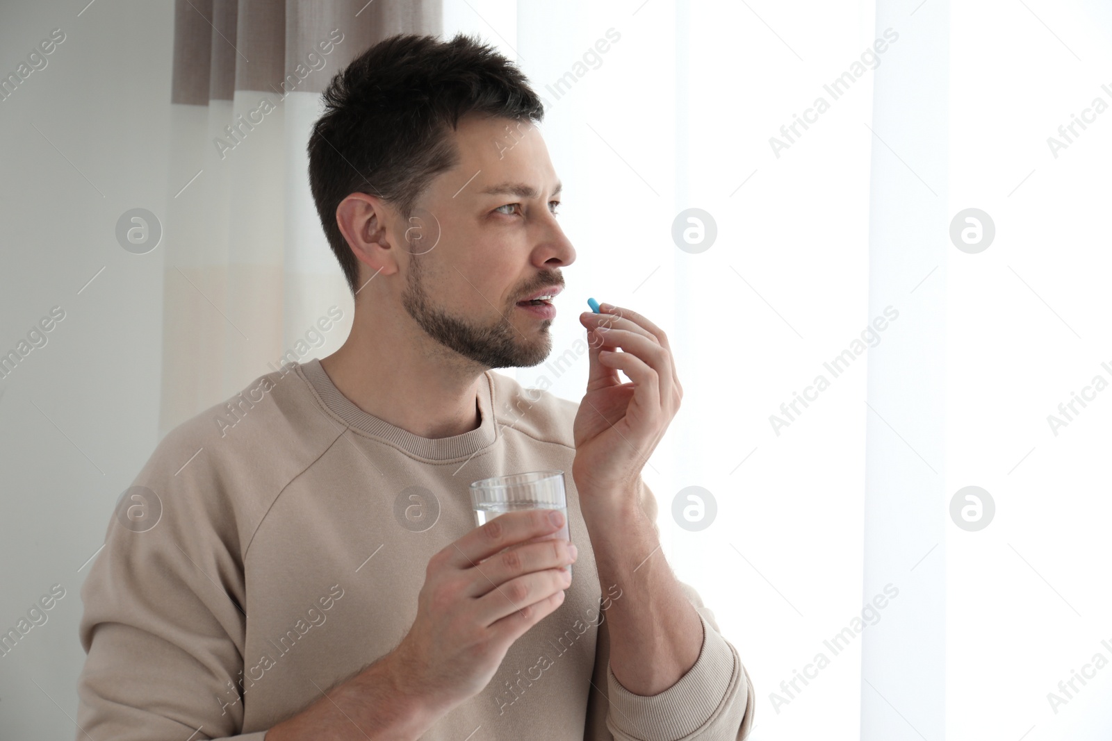 Photo of Man with glass of water taking pill at home