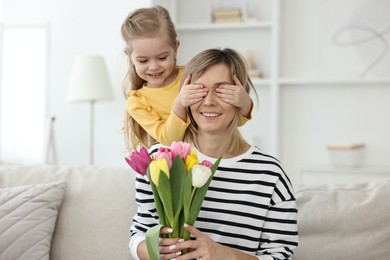Little girl surprising her mom with bouquet of tulips at home. Happy Mother`s Day