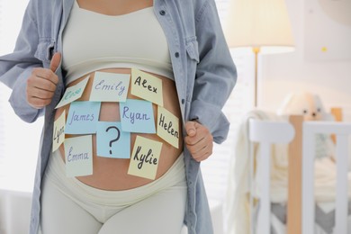 Photo of Pregnant woman with different baby names on belly at home, closeup. Space for text