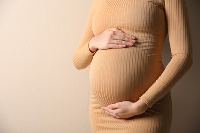 Pregnant woman touching her belly on beige background, closeup