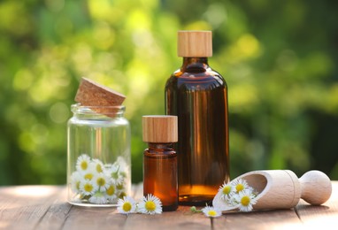 Photo of Bottles of chamomile essential oil and flowers on wooden table