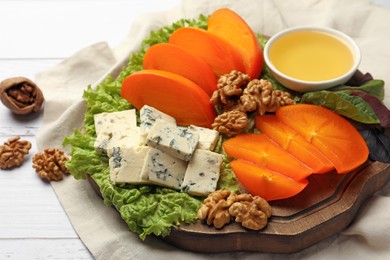 Photo of Delicious persimmon, blue cheese, nuts and honey served on white wooden table