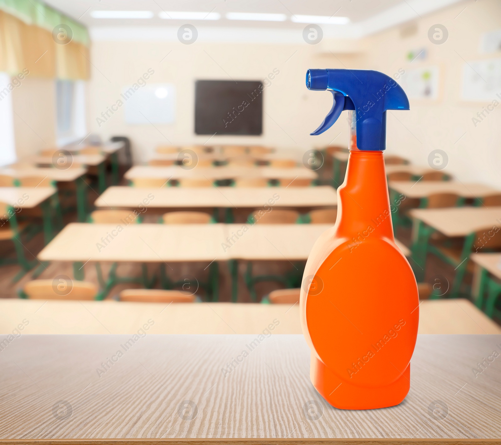 Image of Protective measures during Coronavirus pandemic. Bottle of disinfectant on table against classroom, space for text