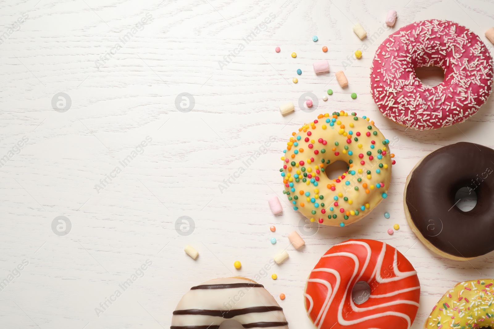 Photo of Delicious glazed donuts on white wooden table, flat lay. Space for text