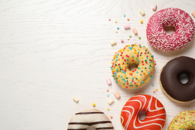 Photo of Delicious glazed donuts on white wooden table, flat lay. Space for text