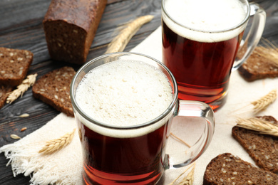 Photo of Mugs of delicious kvass, spikes and bread on table