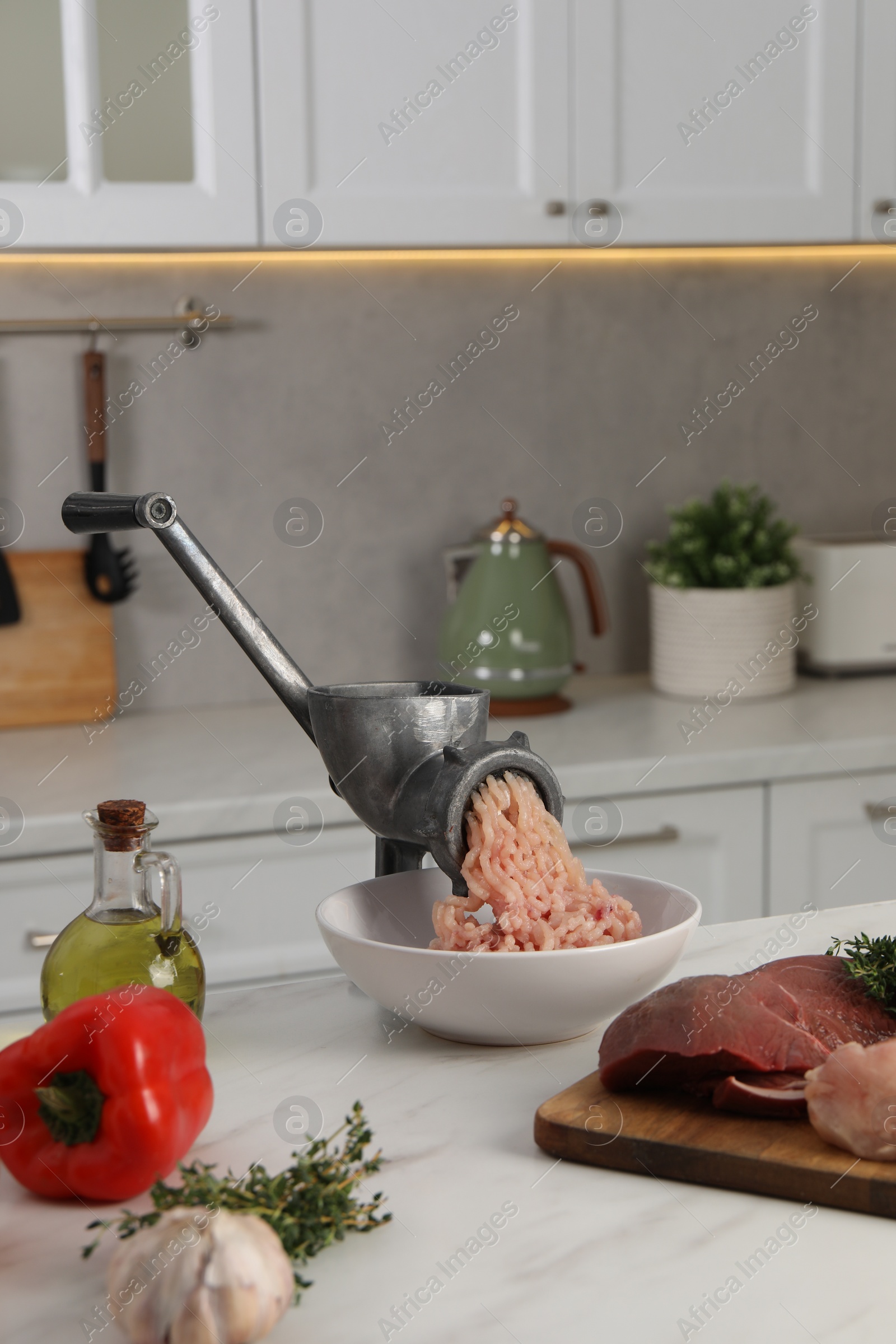 Photo of Metal meat grinder with chicken mince and products on white marble table in kitchen