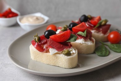 Photo of Delicious sandwiches with bresaola, cream cheese, olives and tomato on light grey table, closeup