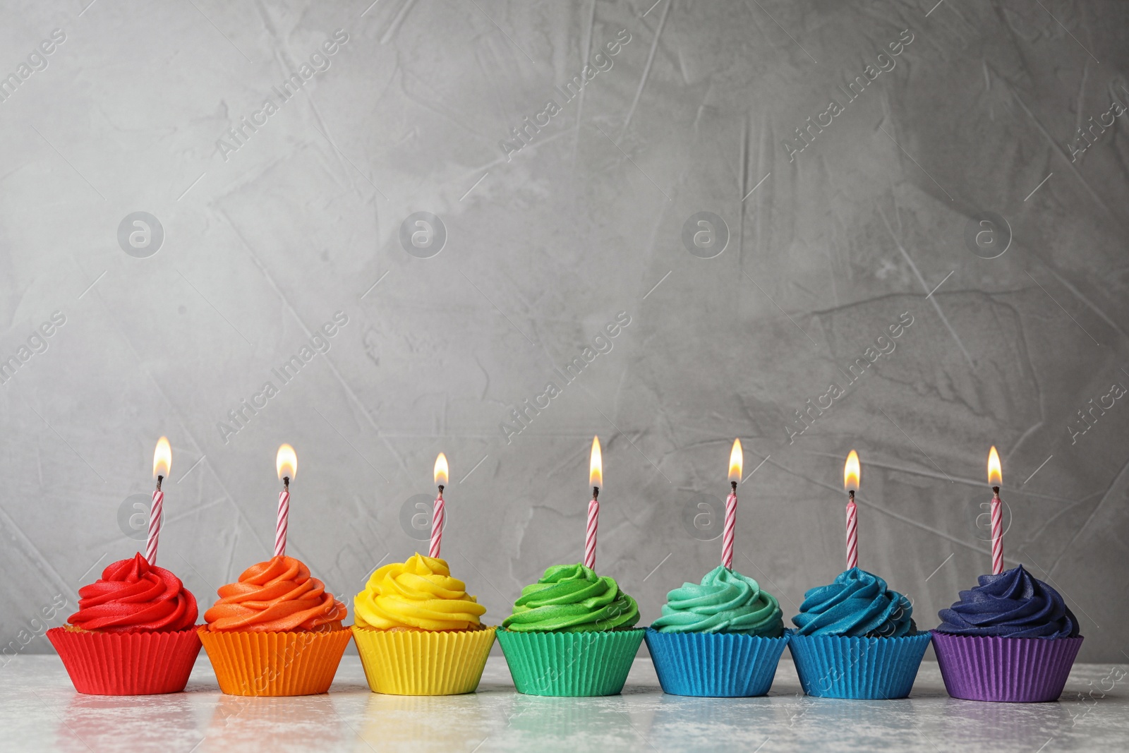 Photo of Delicious birthday cupcakes with burning candles on table