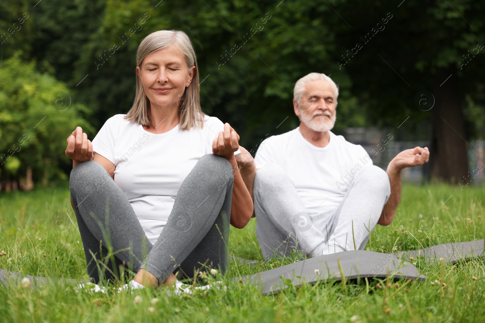 Photo of Senior couple practicing yoga on green grass in park, selective focus