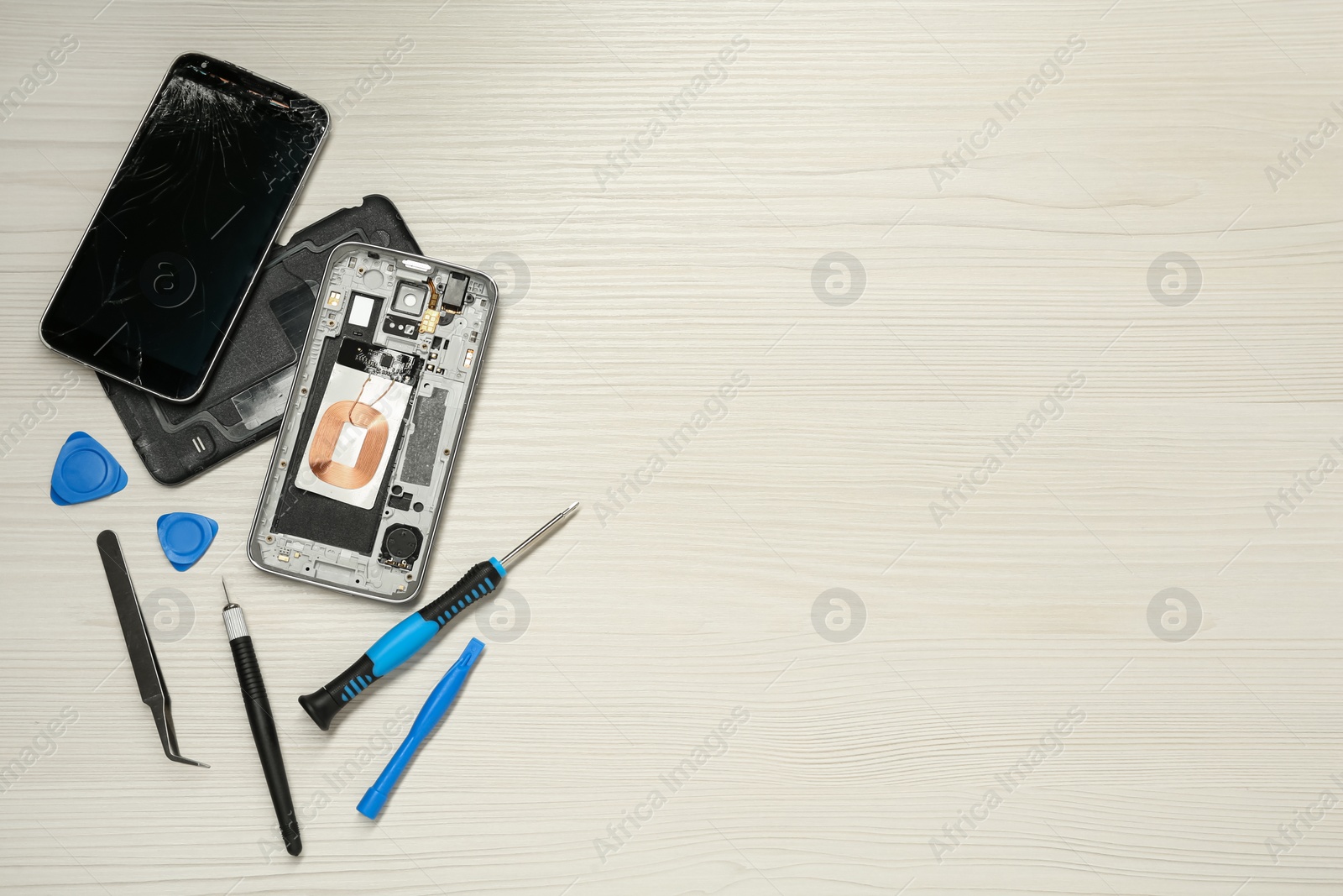 Photo of Damaged smartphone and repair tool set on white wooden background, flat lay. Space for text