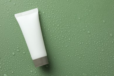 Moisturizing cream in tube on green background with water drops, top view. Space for text