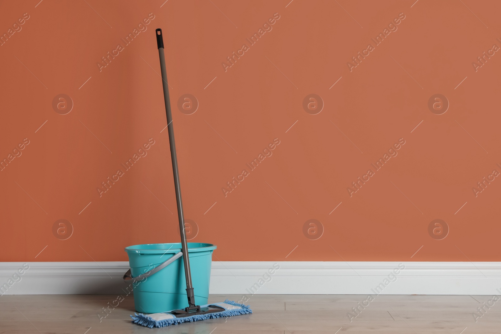 Photo of Mop and bucket on floor near orange wall, space for text. Cleaning service