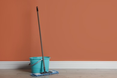 Photo of Mop and bucket on floor near orange wall, space for text. Cleaning service