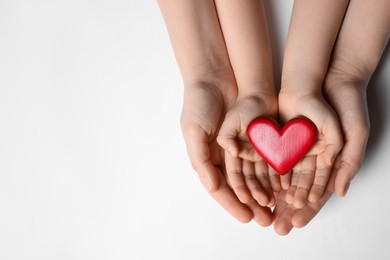 Photo of Woman and kid holding red heart in hands on white background, top view