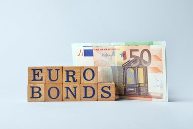 Photo of Word Eurobonds made of wooden cubes with letters and banknotes on light grey background