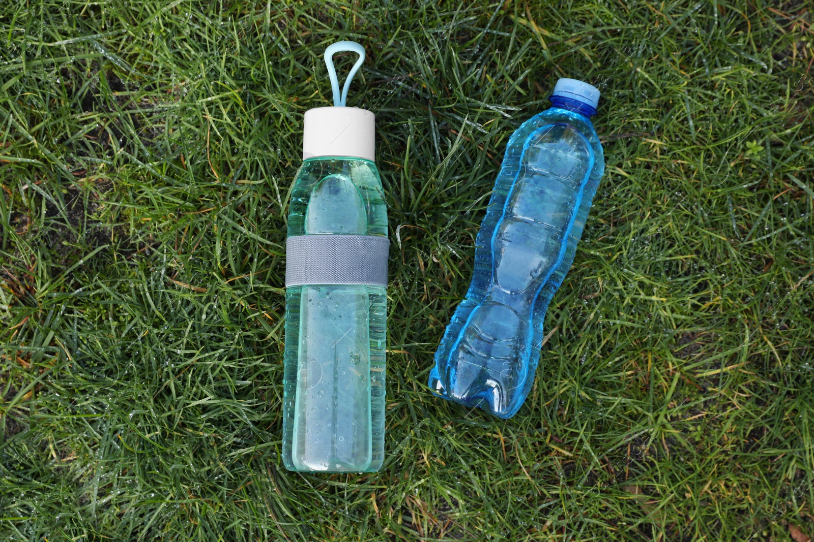 Photo of Bottles of fresh water on green grass outdoors, flat lay