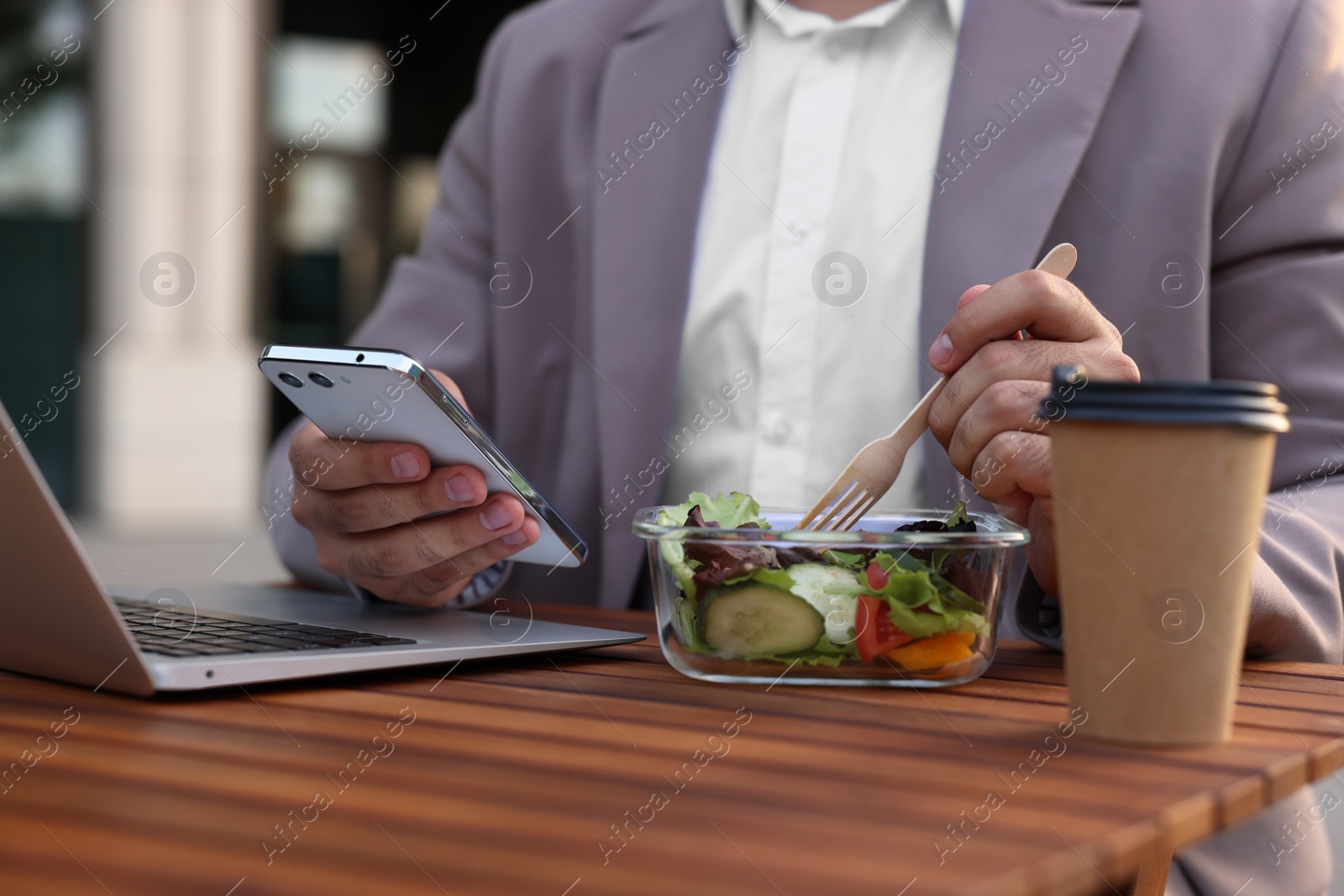 Photo of Businessman using smartphone during lunch at wooden table outdoors, closeup