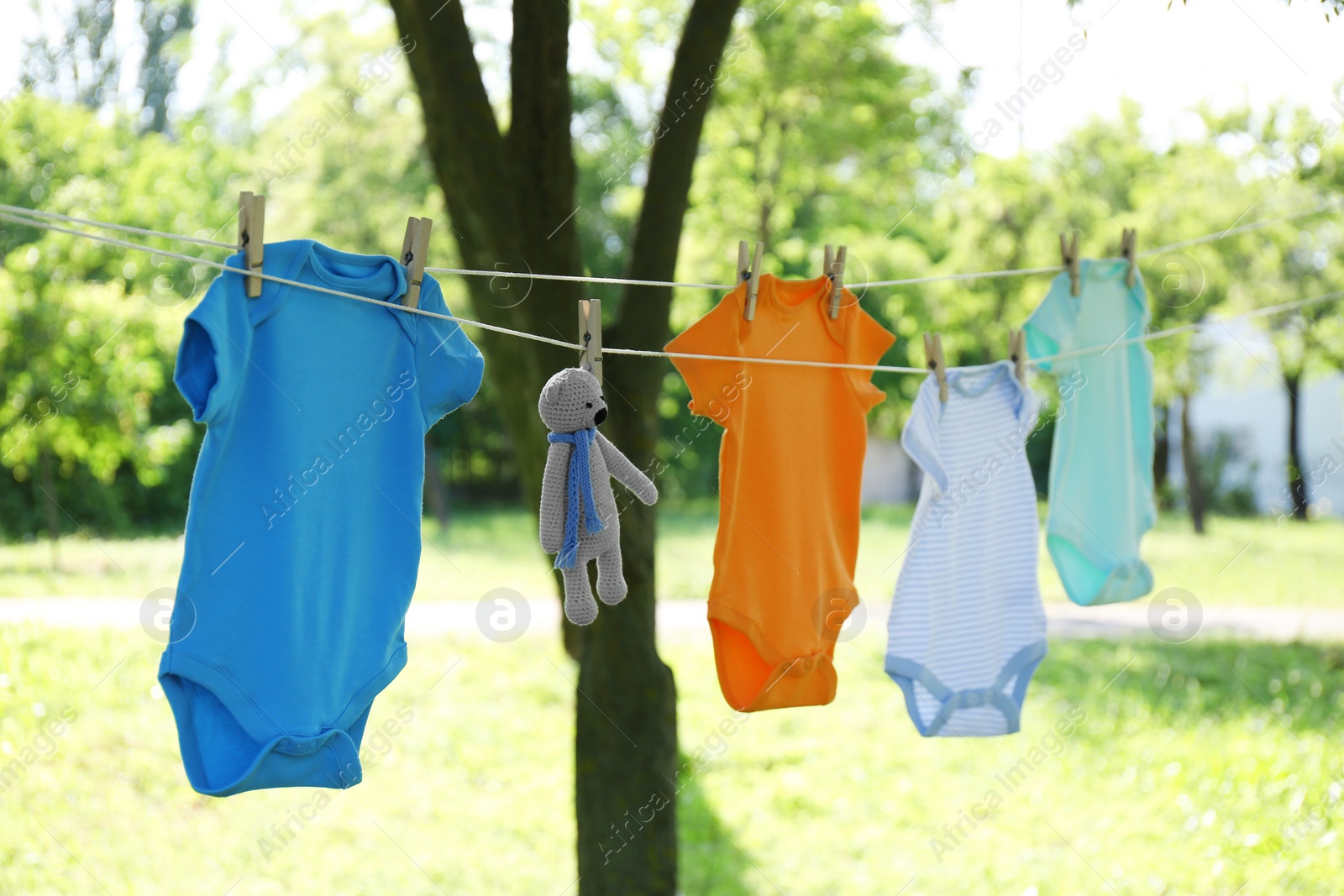 Photo of Colorful baby onesies and toy bear hanging on clothes line outside