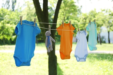 Photo of Colorful baby onesies and toy bear hanging on clothes line outside