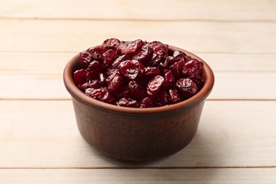 Tasty dried cranberries in bowl on light wooden table, closeup